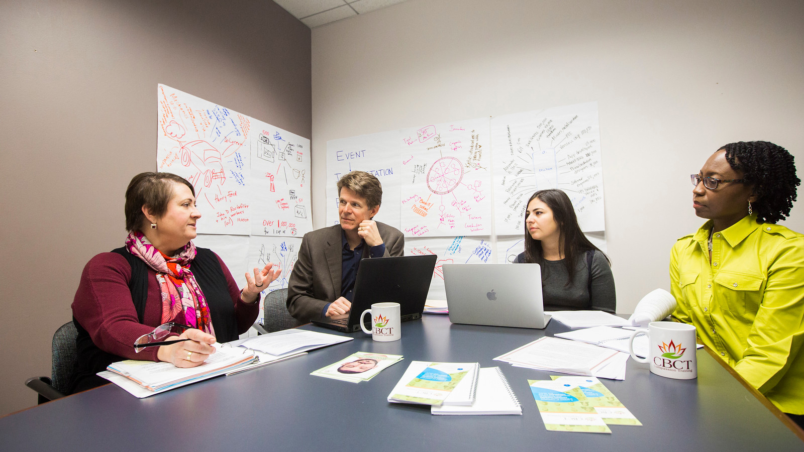 faculty sitting at a table in front of a whiteboard with colorful writing 